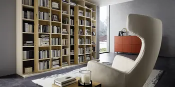 Hohes Bücherregal aus Holz, weißer Sessel und rotes Sideboard in modernem Wohnraum